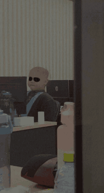 a person wearing sunglasses sits at a desk in front of a hp laptop