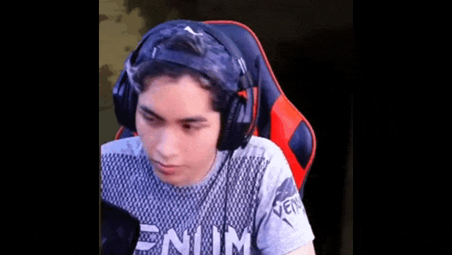 a young man wearing headphones and a shirt that says venum is sitting in a chair .