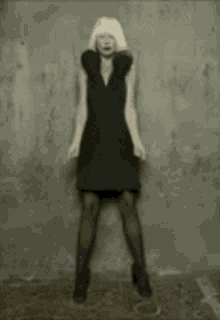 a woman in a black dress is standing in front of a gray wall