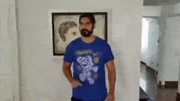 a man with a beard is wearing a blue t-shirt with a mario on it .