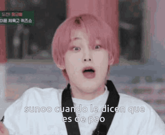 a young man with pink hair is wearing a white shirt and a black belt and making a funny face .