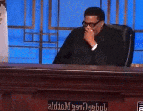 a man is sitting at a judge 's bench with his hand on his mouth .