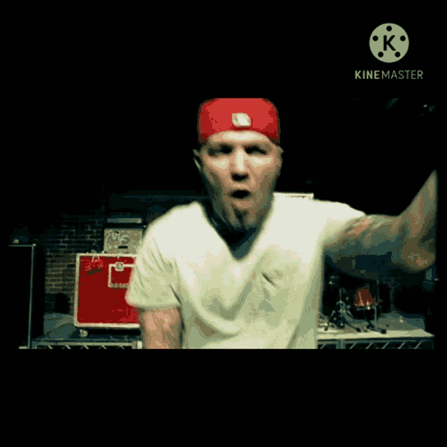 a man wearing a red hat and a white shirt is standing in front of a drum set .