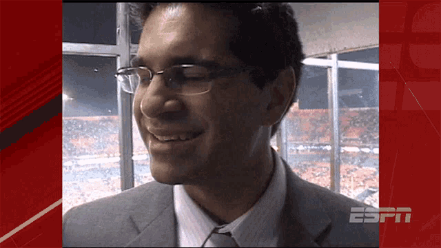 a man wearing glasses and a suit is smiling in front of a espn logo