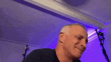 a man is smiling in front of a purple wall