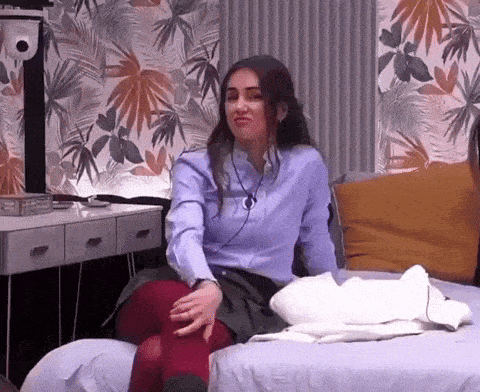 a woman in a blue shirt and red tights is sitting on a bed in a room .
