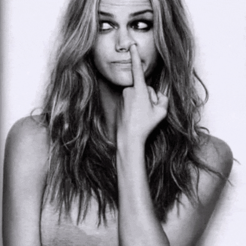 a woman is holding her finger to her nose and making a face .