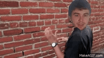 a man is standing in front of a brick wall with his hands up .
