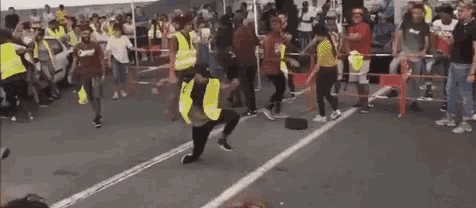 a man in a yellow vest is kneeling down in front of a crowd of people .
