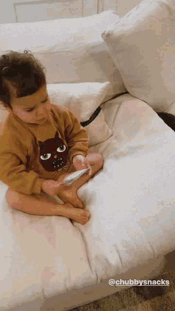 a little girl is sitting on a couch with a cat on her sweater