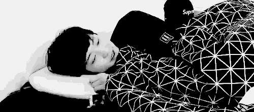 a black and white photo of a person sleeping on a bed covered in a blanket .