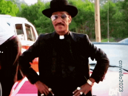 a man wearing a hat and sunglasses is standing with his hands on his hips