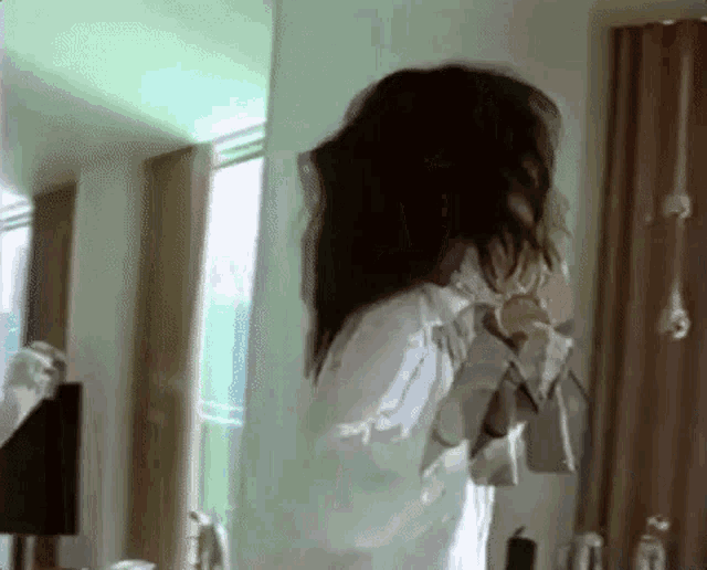 a woman with long hair is standing in front of a mirror in a room .