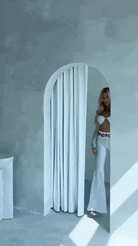 a woman stands in a room with a white curtain
