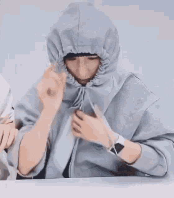 a person wearing a hoodie with a hood on their head is sitting at a table .