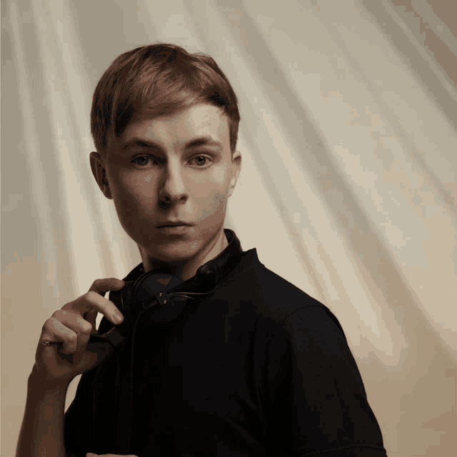 a young man in a black shirt is holding a pair of headphones