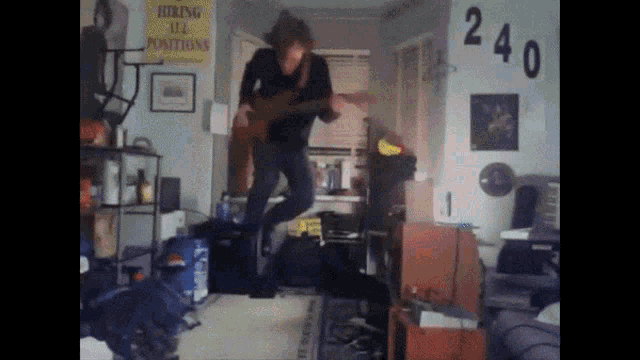 a man jumps in the air while playing a guitar in front of a sign that says " hiring all positions "