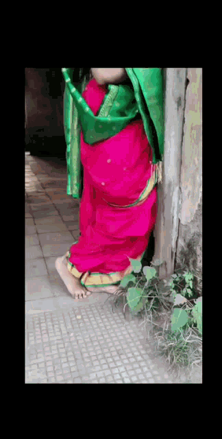a woman in a red and green sari is standing next to a pole