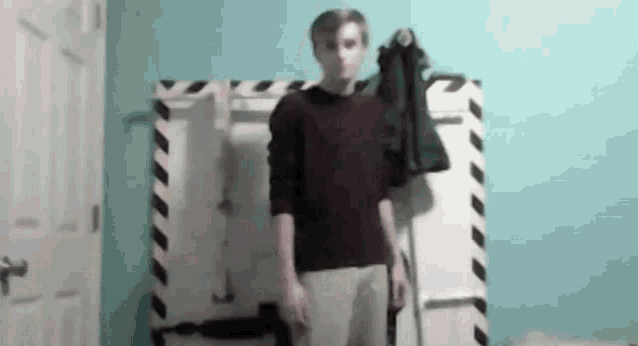 a man in a red sweater and white pants is standing in front of a striped wall .
