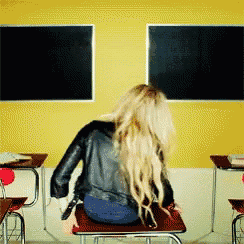 a woman is sitting at a desk in front of a blackboard