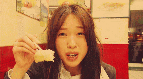 a young woman is eating a piece of food with chopsticks .