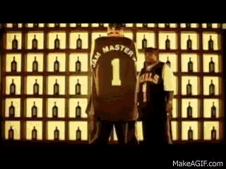 a man wearing a jersey with the number 1 on it stands in front of a wall of bottles
