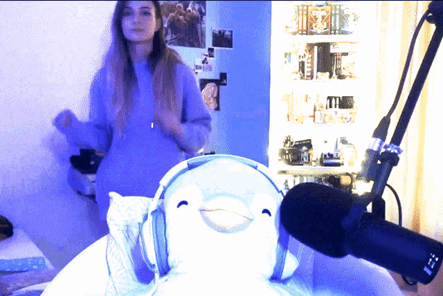 a woman wearing headphones stands in front of a microphone and a stuffed penguin