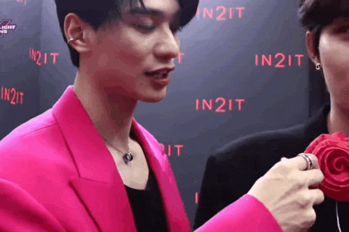 a man in a pink jacket is holding a red rose and talking to another man .