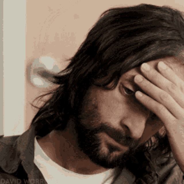 a man with long hair and a beard is covering his face
