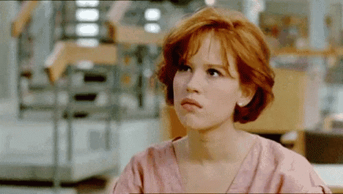 a woman with red hair and a pink shirt is sitting at a table .