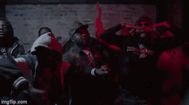 a group of men are dancing in a dark room in front of a brick wall .