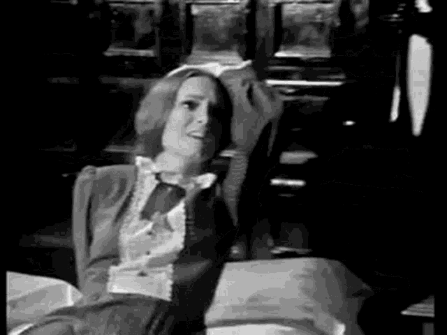 a black and white photo of a woman sitting on a bed holding her head .