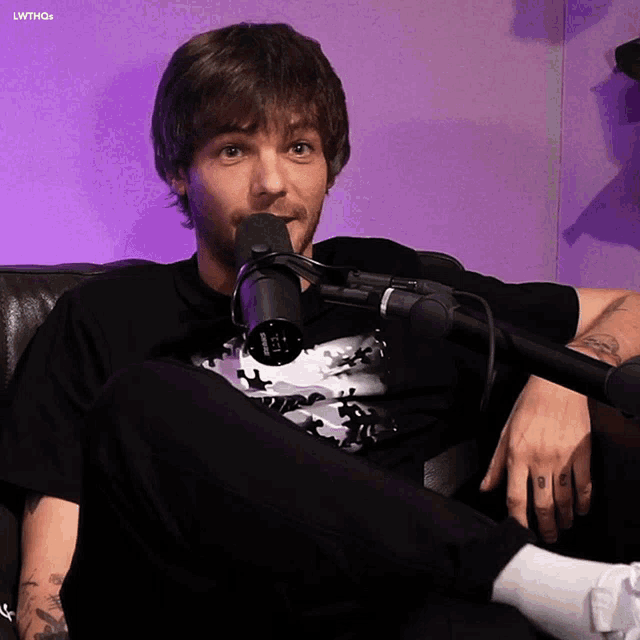 a man is sitting on a couch with a microphone in front of him and a purple background with the letters lwthgs