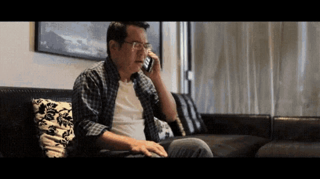 a man sitting on a couch talking on a phone