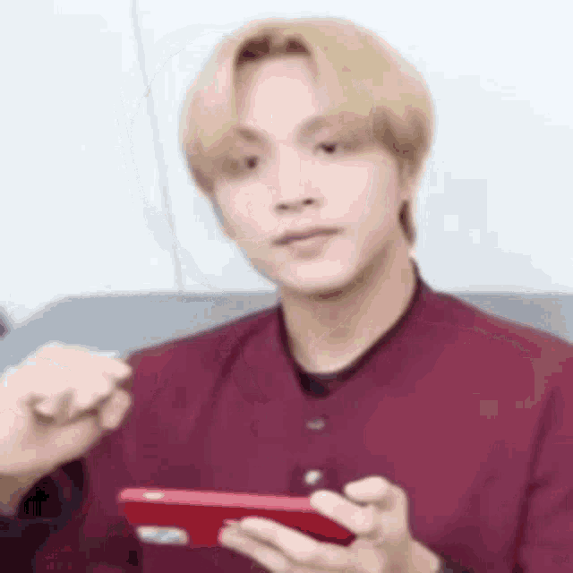 a man is sitting on a couch holding a red cell phone .