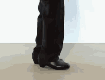 a person wearing black pants and black shoes is standing on a white surface .