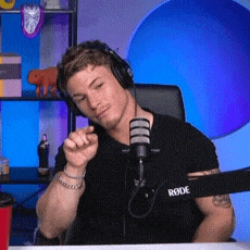 a man wearing headphones is sitting in front of a microphone and pointing at the camera .