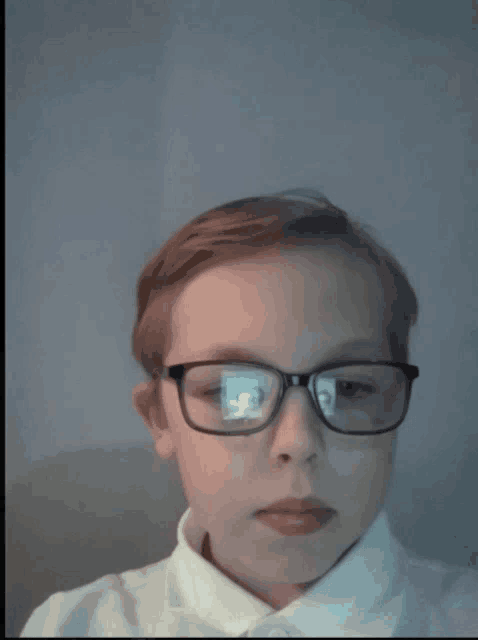 a young boy wearing glasses and a white shirt is looking at the camera