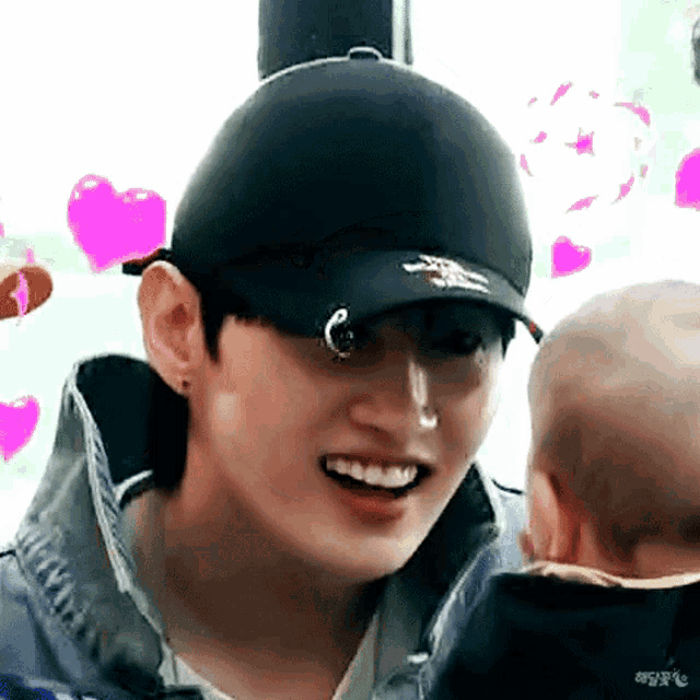 a young man wearing a hat is holding a baby and smiling .