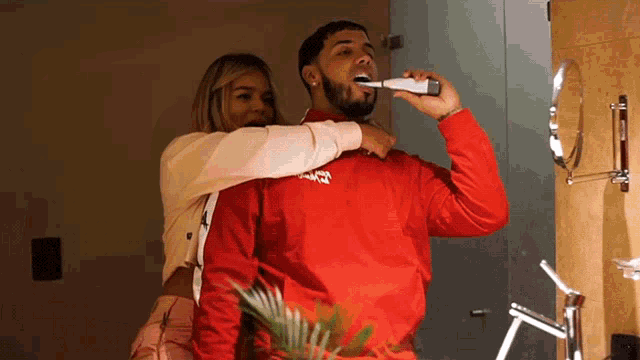 a man is brushing his teeth while a woman holds him