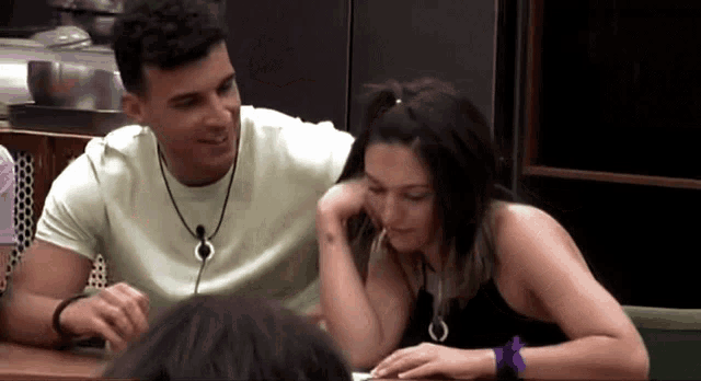 a man and a woman are sitting at a table and the woman has a tattoo on her arm