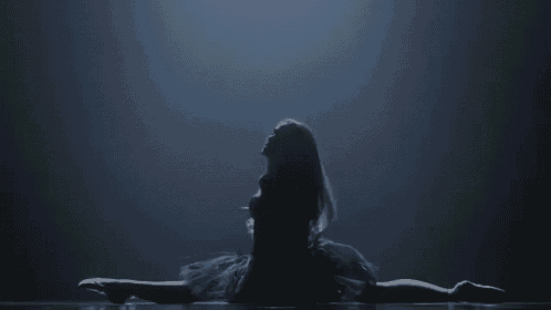 a ballerina is doing a split on the floor in a dark room .