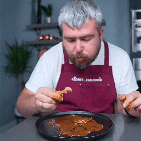 a man wearing an apron that says albert cancook eating a piece of food