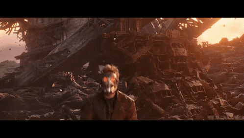 a man in a mask stands in front of a pile of rubble
