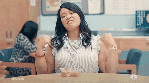 a woman is sitting at a table with her arms outstretched and a bowl of food on her lap .
