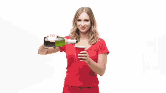 a woman in a red shirt pouring a bottle of wine into a red cup