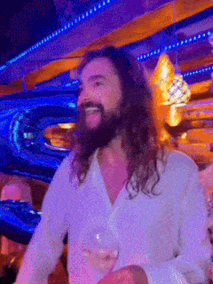 a man with long hair and a beard is holding a glass of wine in a restaurant .