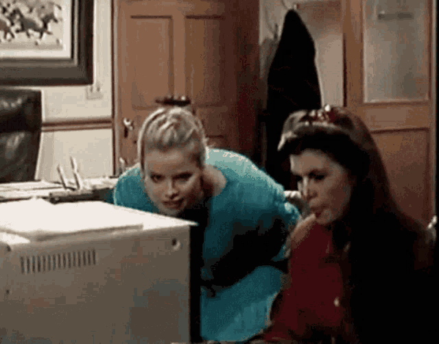 two women are looking at a computer screen and one has a red sweater on
