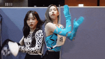 two girls are standing next to each other in a room and one of them is wearing blue gloves .