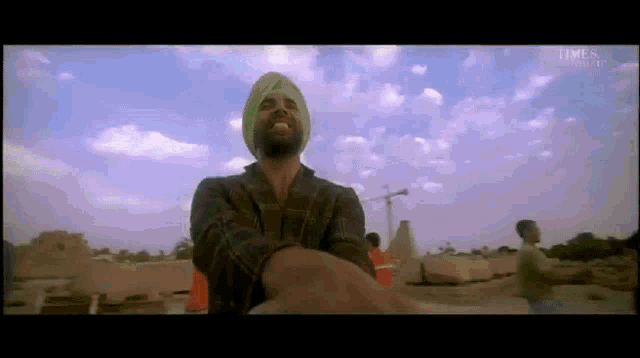 a man wearing a green turban is standing in front of a cloudy sky
